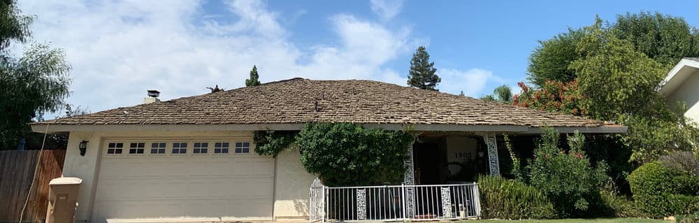 Single-story home with a textured roof and lush greenery, vibrant sky in the background.